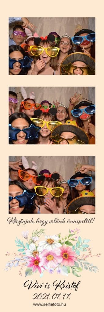 Fotóautomata bérlés. Vidám fiatalok egy selfiebox előtt pózolnak esküvői rendezvényen, színes óriás szemüvegekkel, vicces fejdíszekkel és kiegészítőkkel. A háttér elegáns dekorációval és fényfüzérekkel van díszítve. A csoportos fotózás során mindenki felszabadultan nevet, először mókás pózokat vesznek fel.