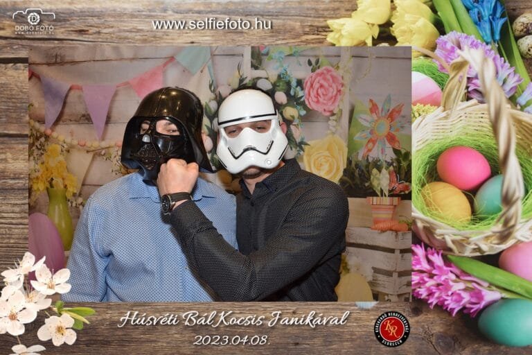 Húsvéti bál fotóbox emlék: két barát Star Wars maszkokban - Darth Vader és Stormtrooper - vidáman pózol, tavaszi virágos-zászlós háttér előtt, húsvéti tojásos és virágos dekoratív kerettel díszítve.