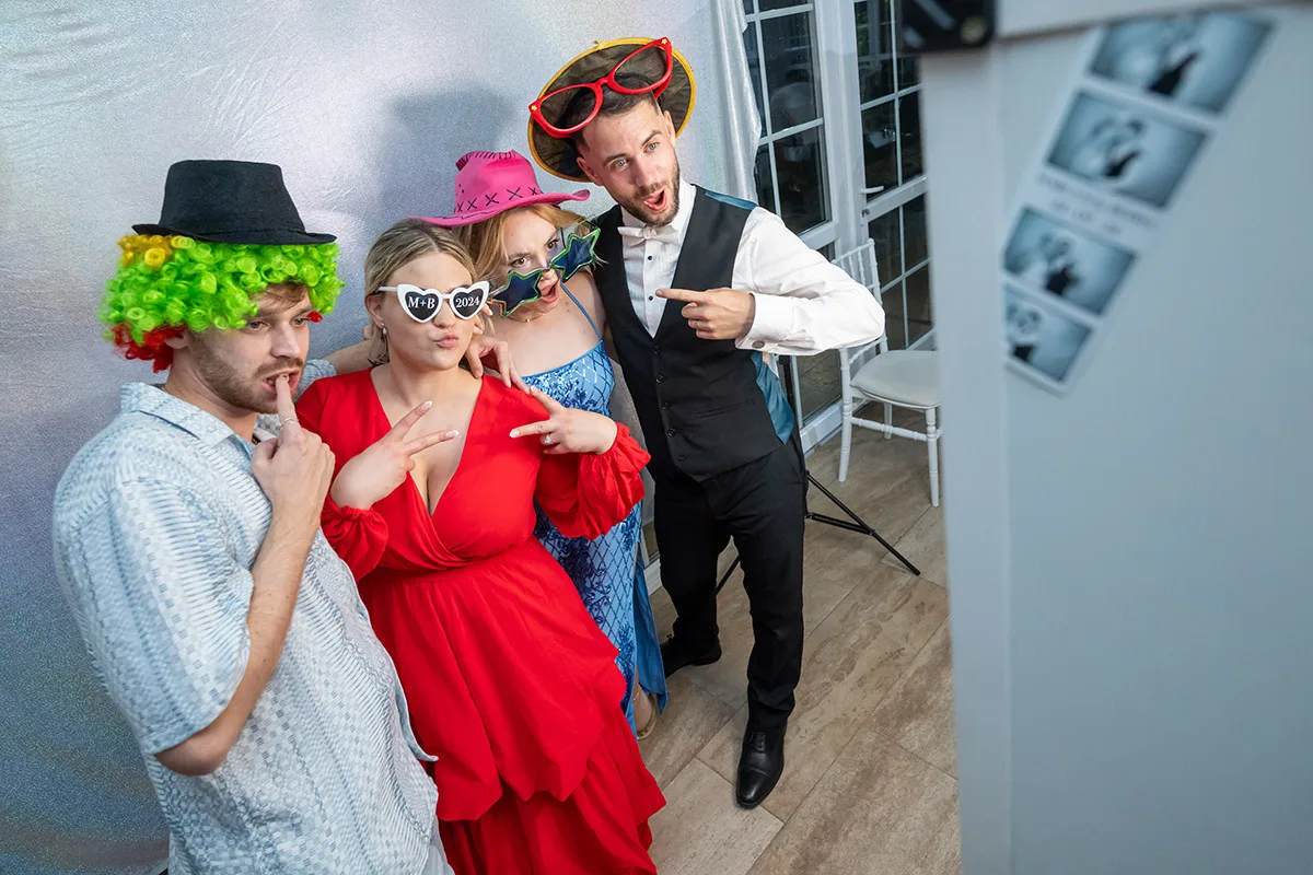 Vidám társaság szelfigépnél, kreatív kiegészítőkkel. A szelfigép szórakoztató és emlékezetes élményt nyújt esküvőkön, bulikon és rendezvényeken Debrecenben.